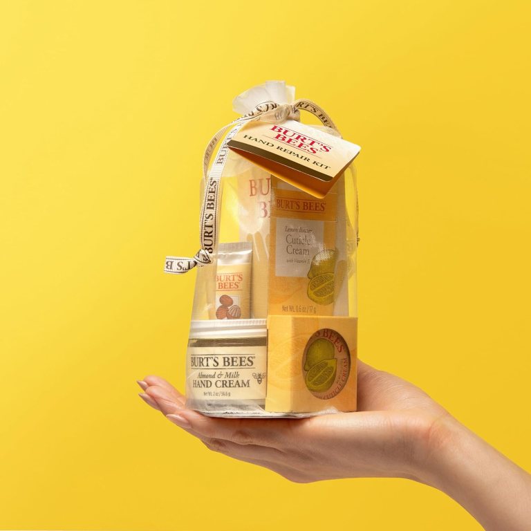 A person holding a Burt's Bees Hand Repair Kit, featuring several skincare products inside a transparent package, against a bright yellow background.