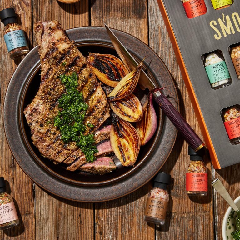 A beautifully plated grilled steak garnished with fresh parsley, accompanied by charred onions, and surrounded by jars of seasoning blends on a rustic wooden table.