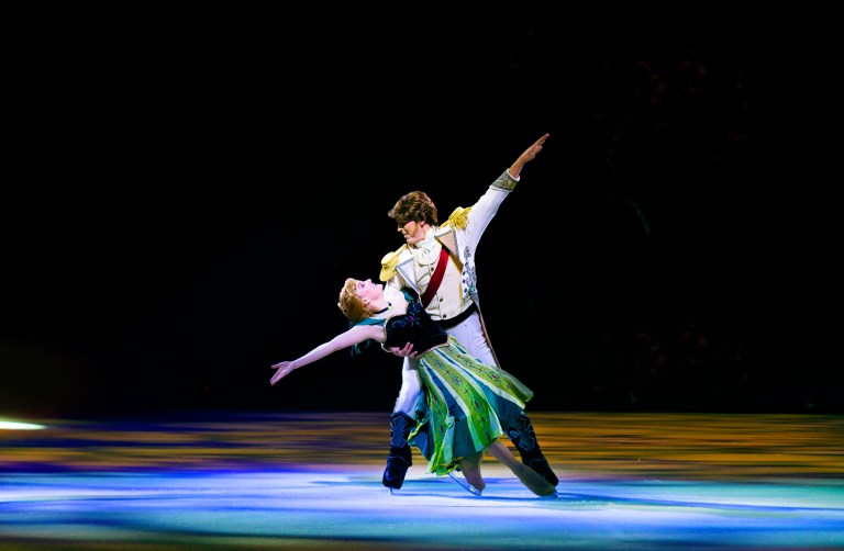 A male and female ice skater perform a graceful dance on ice, with the female skater extending her arm and the male skater supporting her, set against a dramatic, dark background.