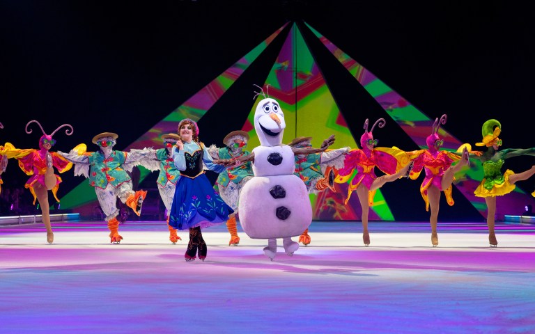 A lively scene from Disney On Ice features characters Anna and Olaf performing on ice, surrounded by colorful performers in vibrant costumes and a bright, visually striking backdrop.
