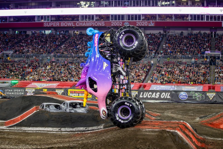 A monster truck performing a wheelie at a Monster Jam event, surrounded by an enthusiastic crowd in a stadium.