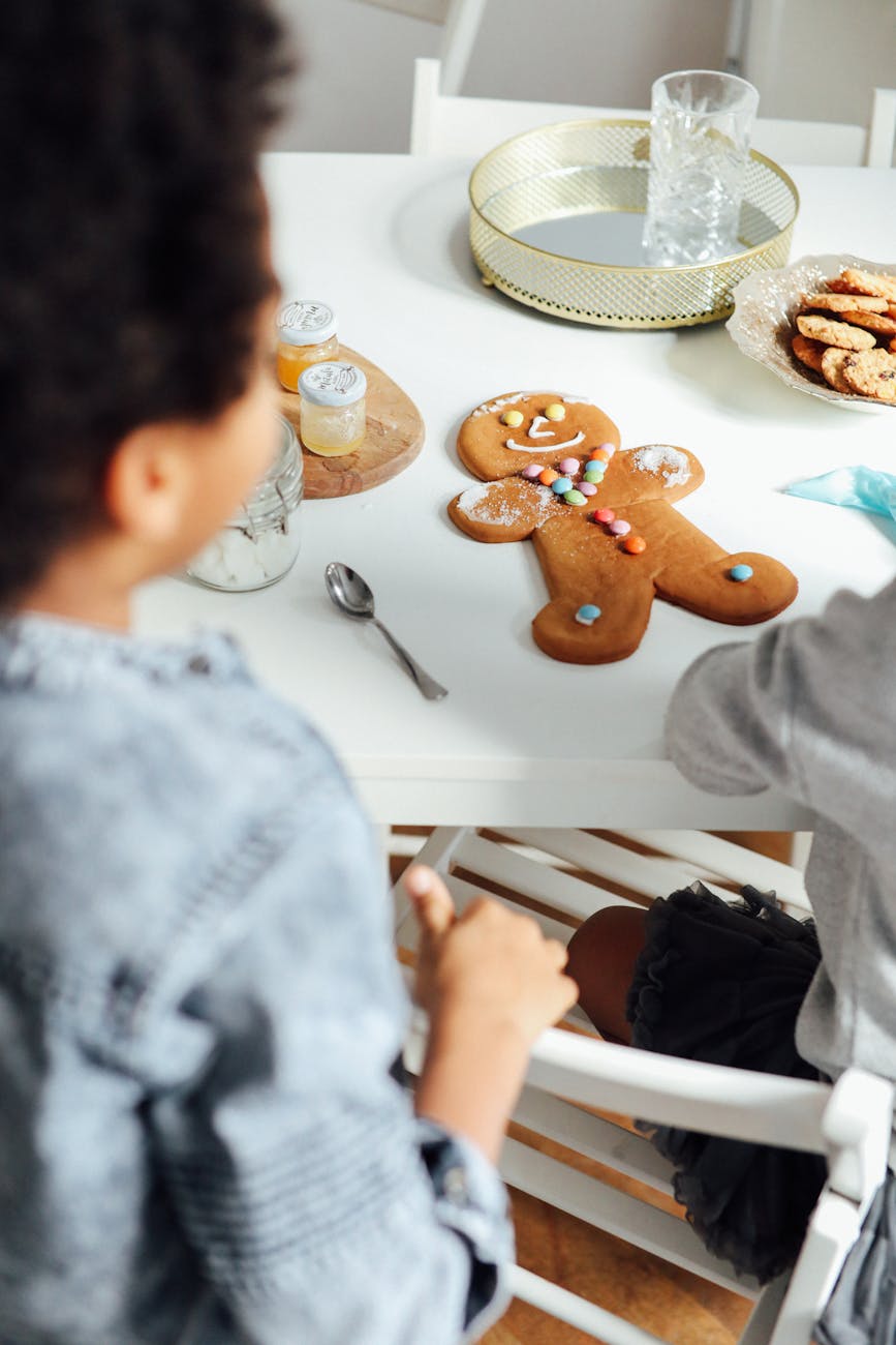 A child decorating a gingerbread cookie with colorful candies and icing, sitting at a table with additional cookies and decorations in the background.