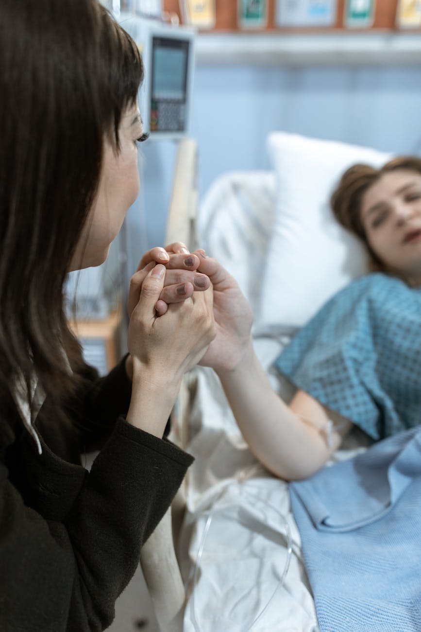 A woman holding the hands of a patient in a hospital bed, showing support and care.