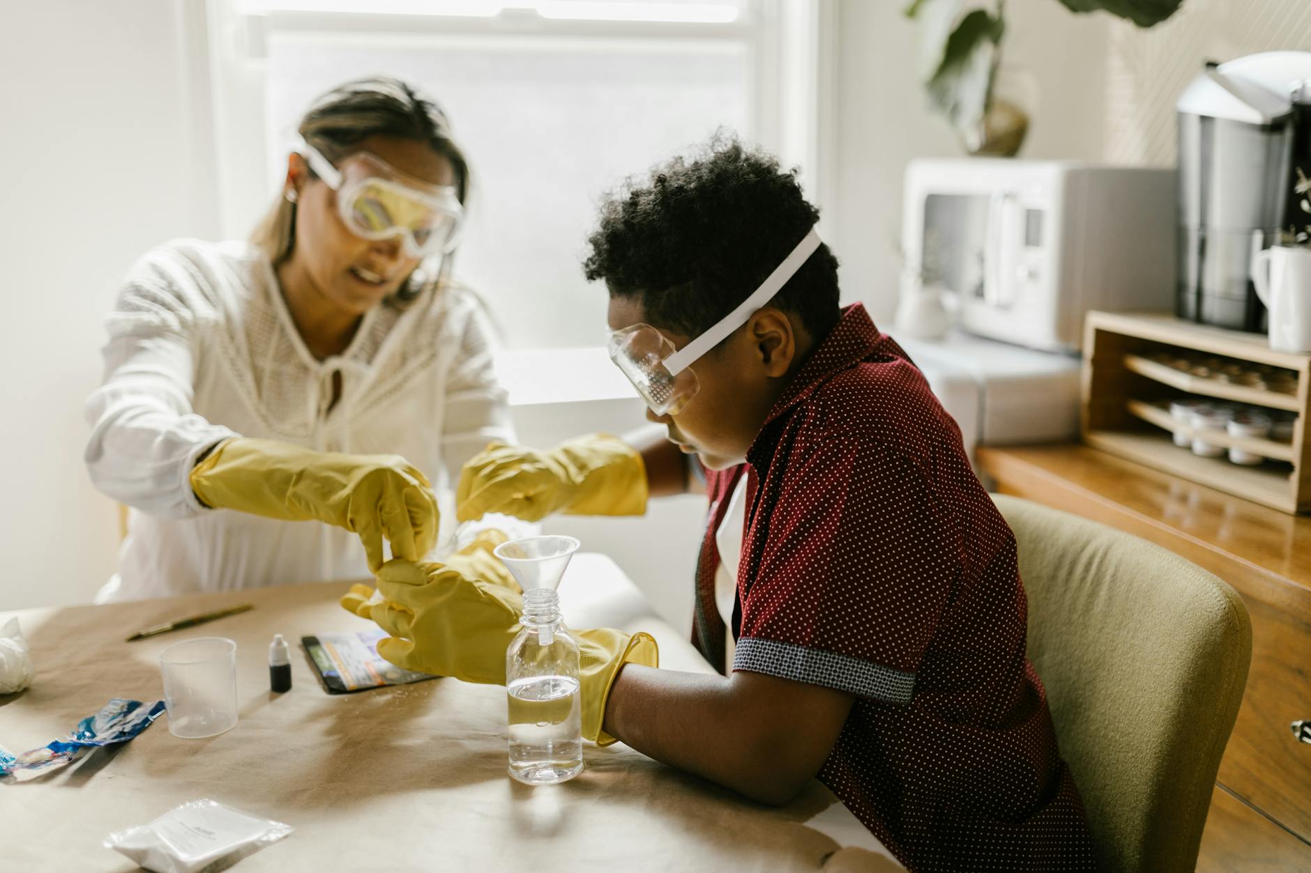 A child and an adult conduct a science experiment together at a table, both wearing safety goggles and rubber gloves, with scientific materials and tools displayed around them.