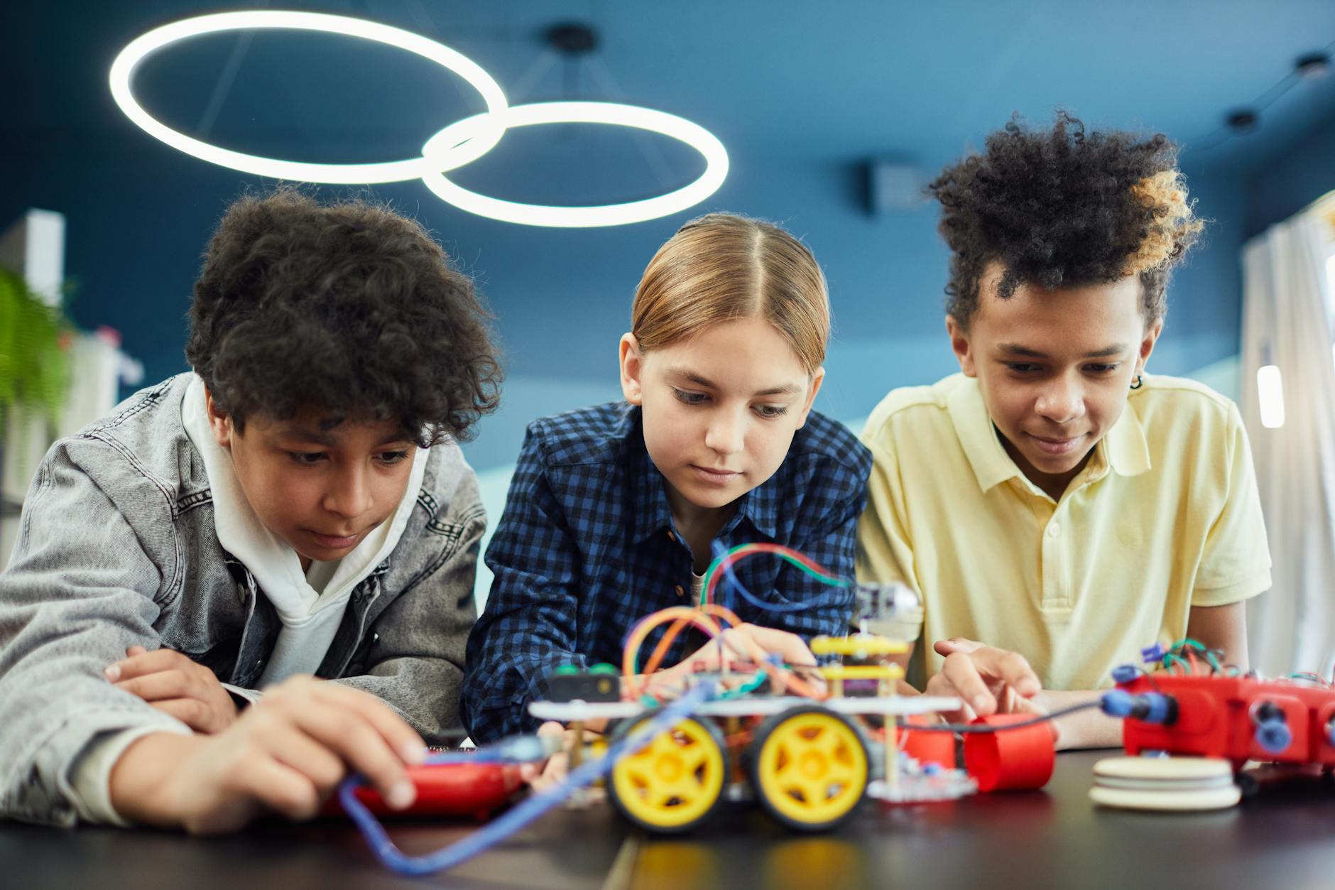 Three children engaged in a hands-on science activity, working together on a robotic project at a table.