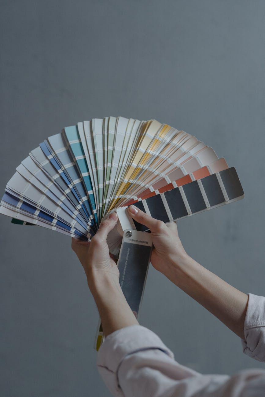 A person holding a fan of paint color swatches, showcasing various shades and hues against a gray background.