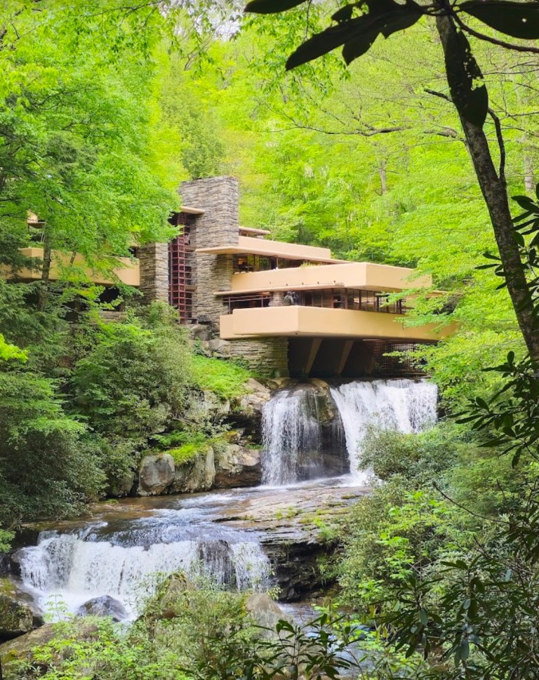 A modern architectural structure built over a waterfall, surrounded by lush green trees and vegetation.