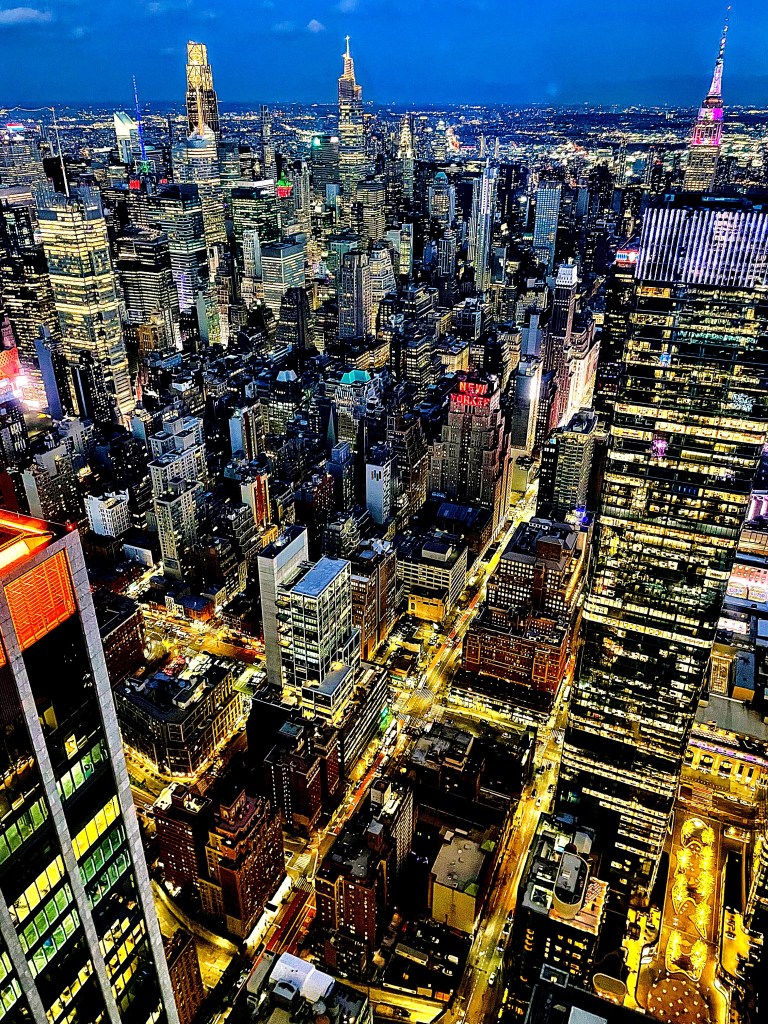Aerial view of a bustling cityscape at night, showcasing illuminated skyscrapers and busy streets.