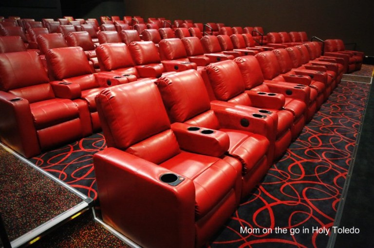 Empty theater seating area featuring rows of red reclining chairs with armrests and cup holders.