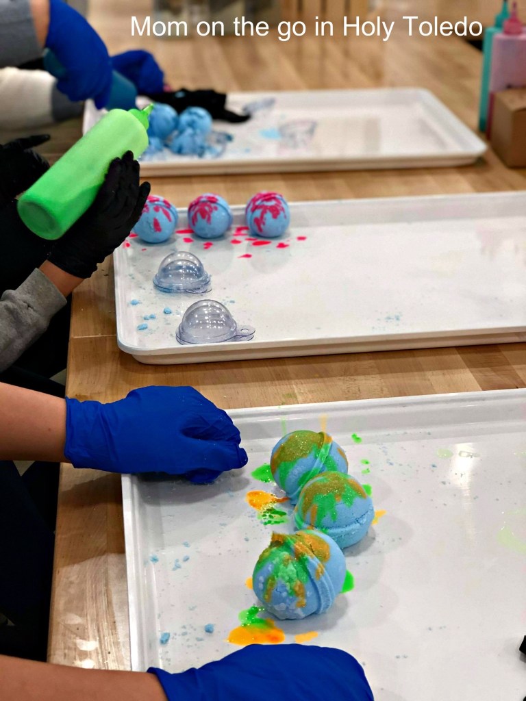 Participants assembling colorful bath bombs on trays, displaying various colors and designs with squirt bottles.