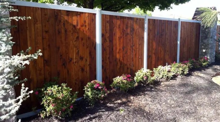 A wooden fence with metal accents, surrounded by a garden of colorful flowers and shrubs on a sunny day.