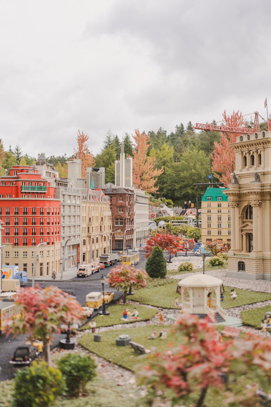 A detailed miniature city model featuring buildings, trees, and tiny figures, with vibrant autumn colors and a cloudy sky.