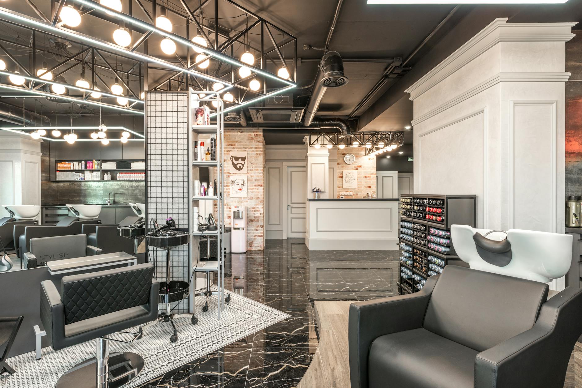 Interior of a modern hair salon featuring stylish black and white furniture, brightly lit with hanging bulbs, and organized workstations with hair products and tools.