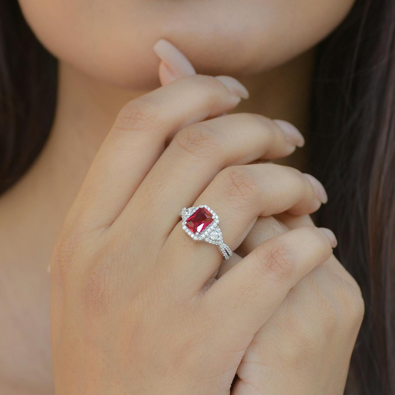 A close-up of a hand wearing a silver ring with a large red gemstone and intricate diamond accents.