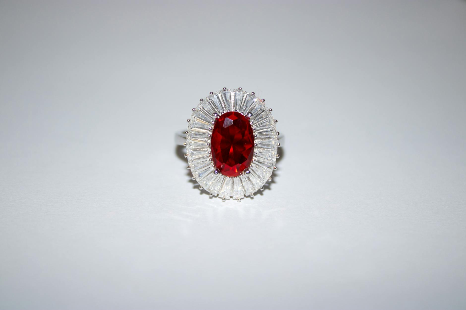 A silver ring featuring a large oval red gemstone surrounded by a halo of diamond-like stones.