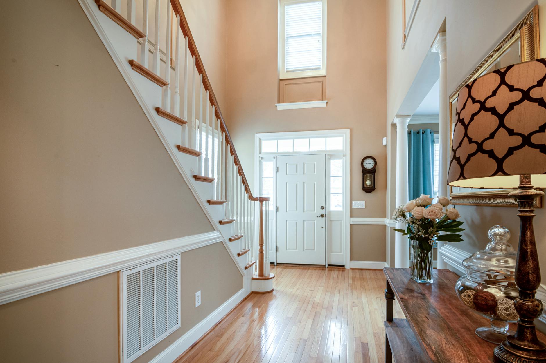 Bright and welcoming hallway featuring a staircase, decorative lamp, and a vase of flowers on a wooden table.