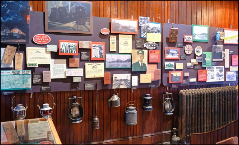 A wall display featuring historical items related to the New York Central Railroad, including photographs, certificates, and various artifacts such as lanterns, showcasing the railroad's history.