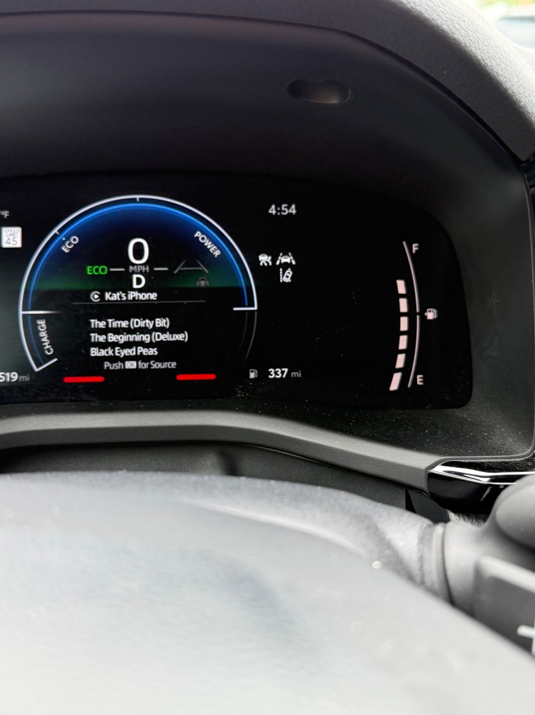 Close-up of a car's dashboard display showing speed, power, and music information, with a time of 4:54 and a remaining range of 337 miles.