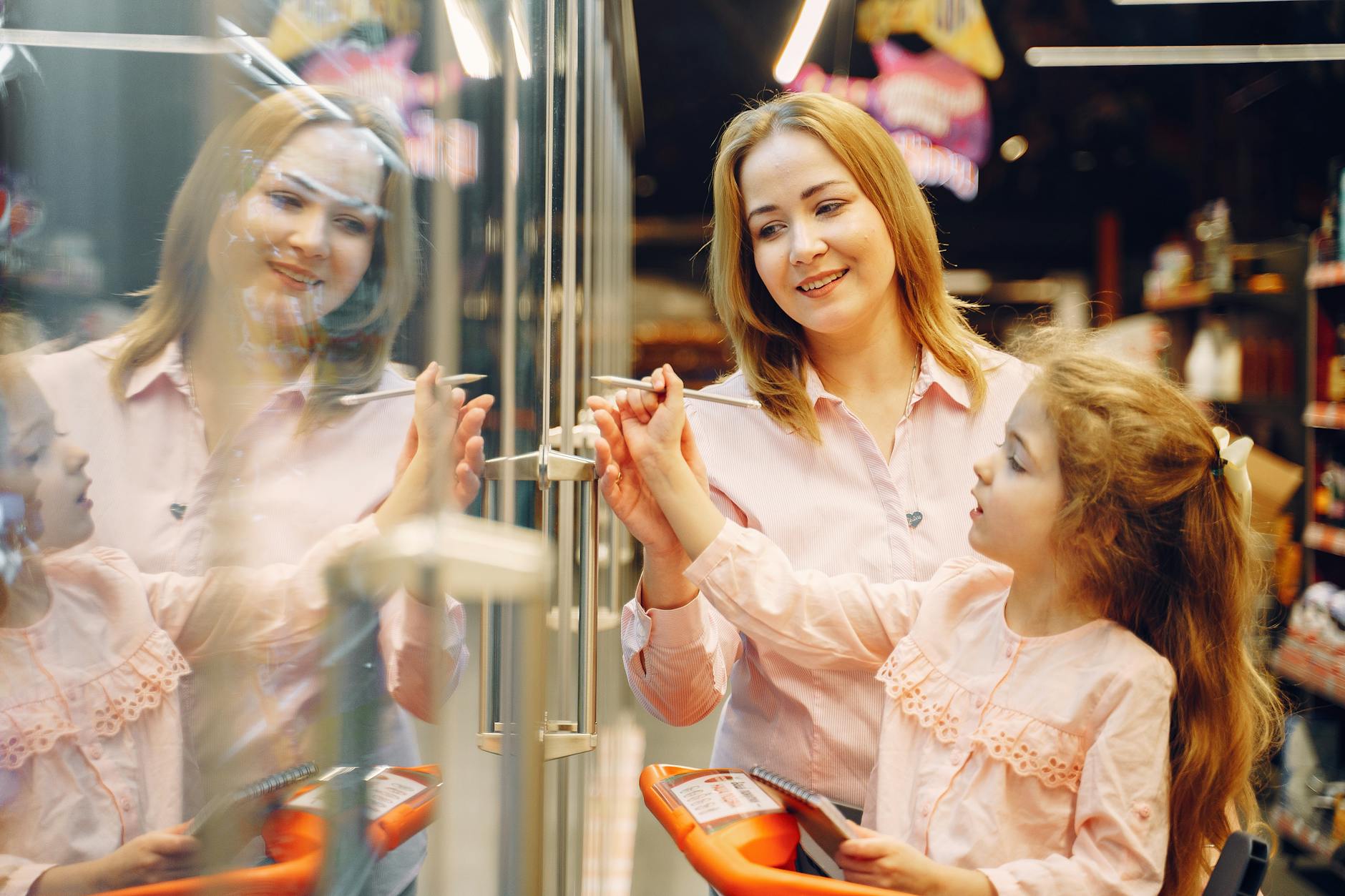 A mother and daughter interact while shopping, with the mother smiling and guiding her child's hand towards a display in a store.