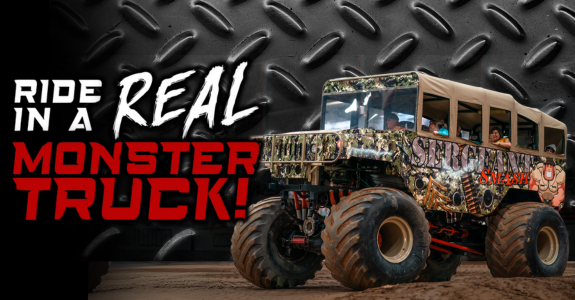 A brightly decorated monster truck with oversized tires, parked against a textured metal background featuring the text 'Ride in a Real Monster Truck!'