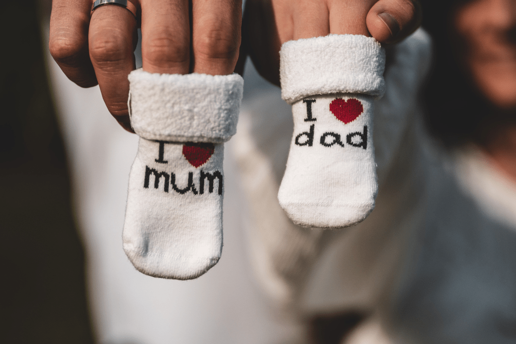 Baby socks with 'I love mum' and 'I love dad' text, held by hands.