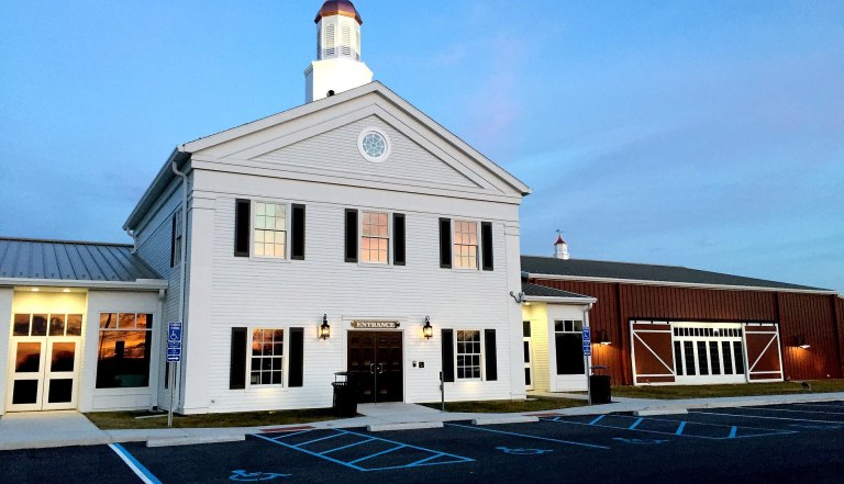 Exterior view of a white, two-story building with a steeple, featuring a sign that says 'Entrance', surrounded by a parking lot with blue lines.