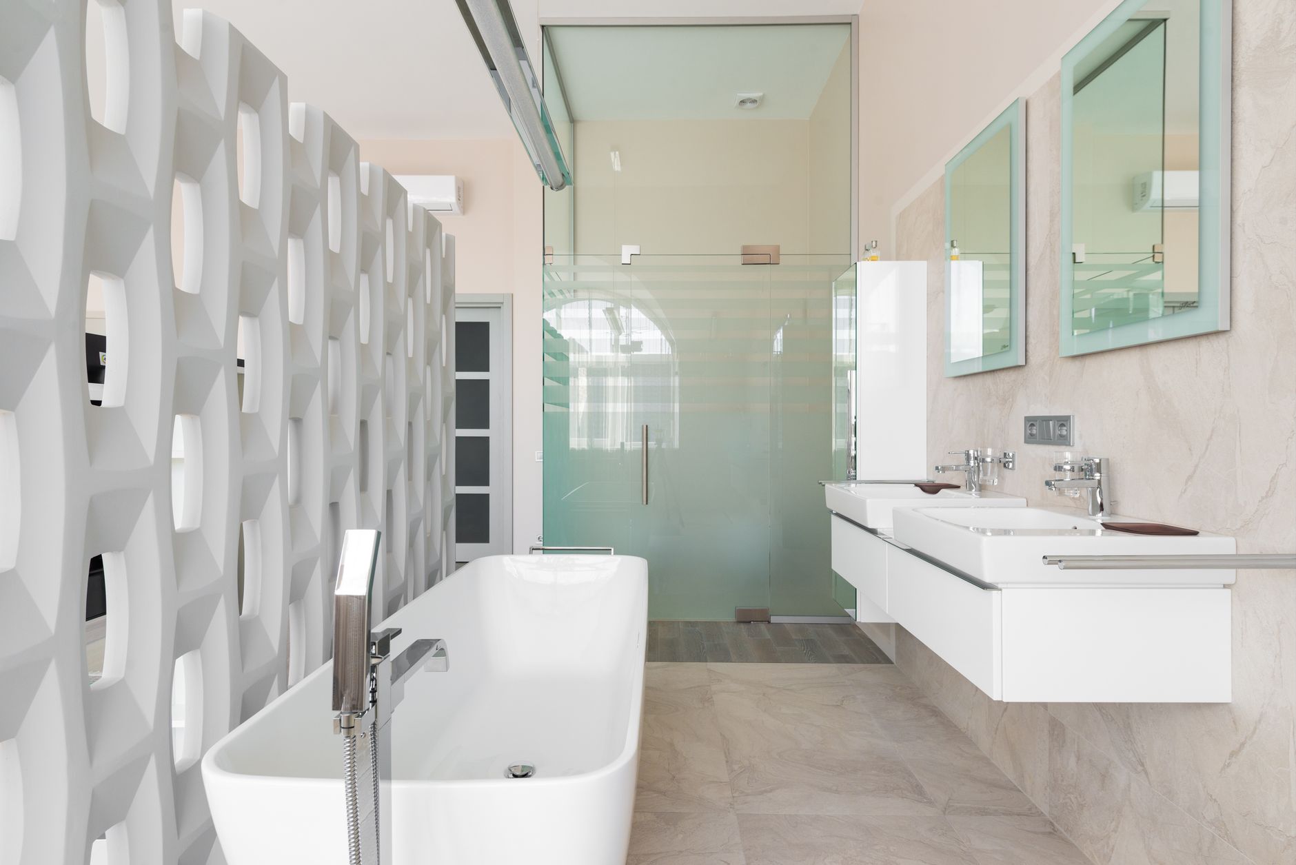 Modern bathroom interior featuring a freestanding bathtub, dual wall-mounted sinks, and a glass shower. Distinctive partition wall with geometric design adds privacy.