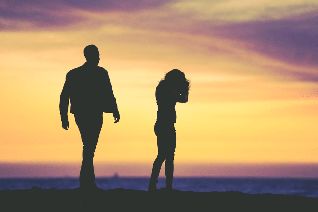 Silhouettes of a man and a woman walking on a beach at sunset, with colorful sky and ocean in the background.