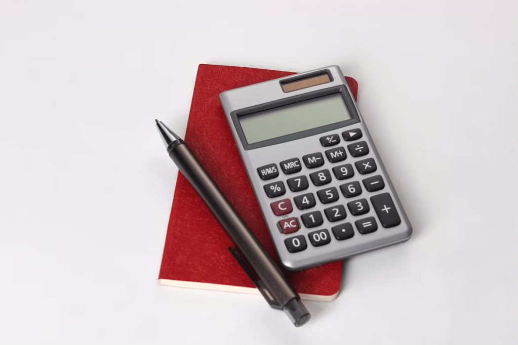 A calculator placed on top of a red notebook, next to a black pen.
