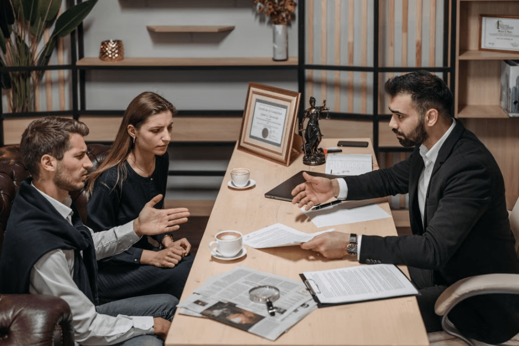 A lawyer discussing important documents with a couple at a table in an office setting, with a decorative statue in the background.