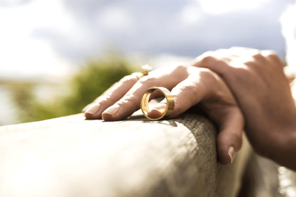 Close-up of a hand resting on a wooden surface, wearing a gold ring.