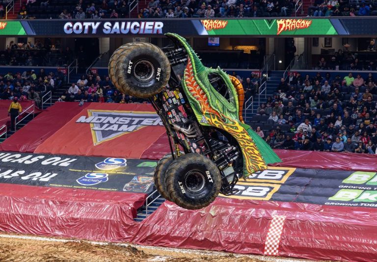 A monster truck performing a wheelie during a live event, showcasing its unique dragon-themed design and large tires.