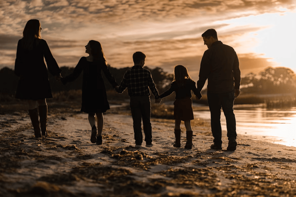 A silhouette of a family walking hand-in-hand along a beach at sunset, with two adults and three children against a colorful sky.