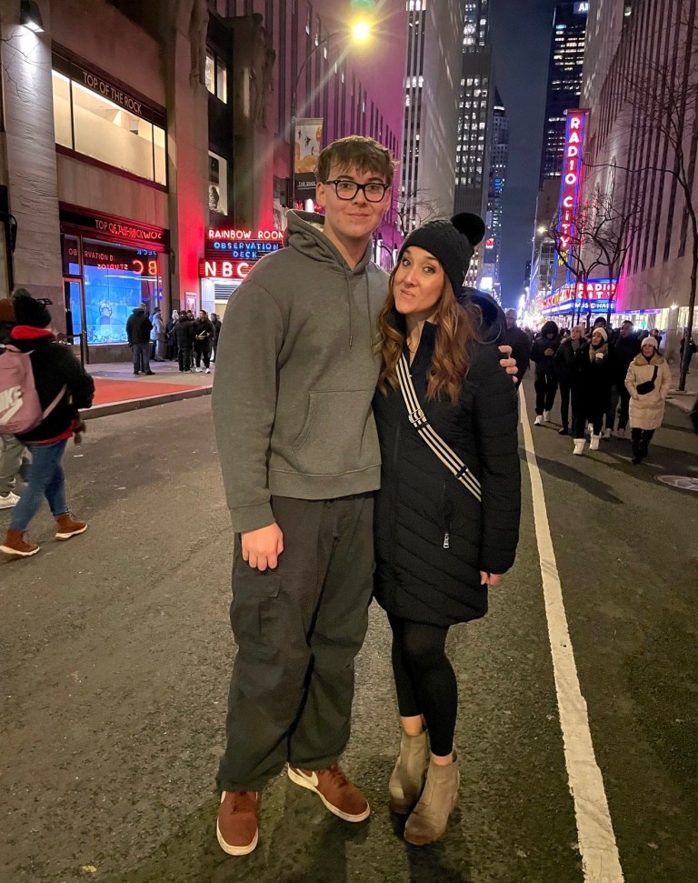 Young man and woman posing for a photo on a busy city street at night, with bright lights and city buildings in the background.