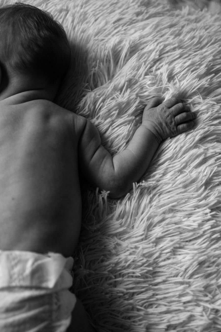 Close-up of a sleeping infant's back and arm resting on a fluffy white blanket.