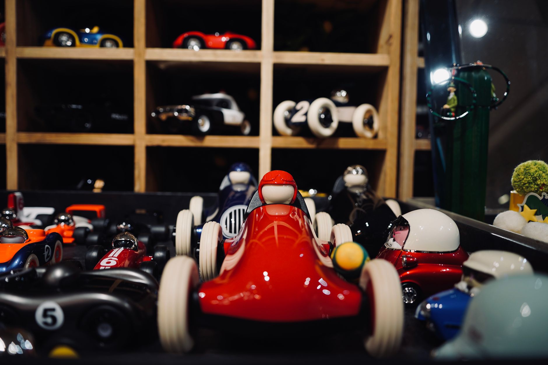 A collection of colorful toy race cars displayed in a wooden box, featuring a prominent red race car in the foreground.